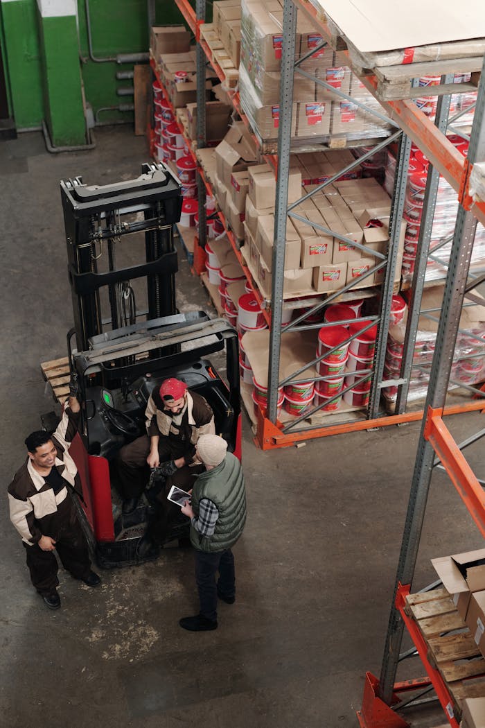 services-04 High-angle view of warehouse employees operating a forklift surrounded by stacked shelves.